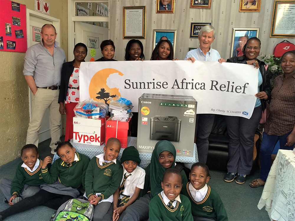 Robert and Paul hold Sunrise Africa Relief banner surrounded by IT donations and schoolchildren from Greenfield Community Primary in Johannesburg