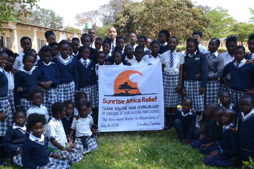 Large group of uniformed school children hold a thank you banner addressed to Sunrise Africa Relief - "We now have water in abundance"